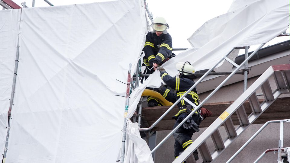 Feuerwehrleute sichern in Hamburg an einem Mehrfamilienhaus Planen an einem Gerüst, die sich durch starken Sturm gelöst haben