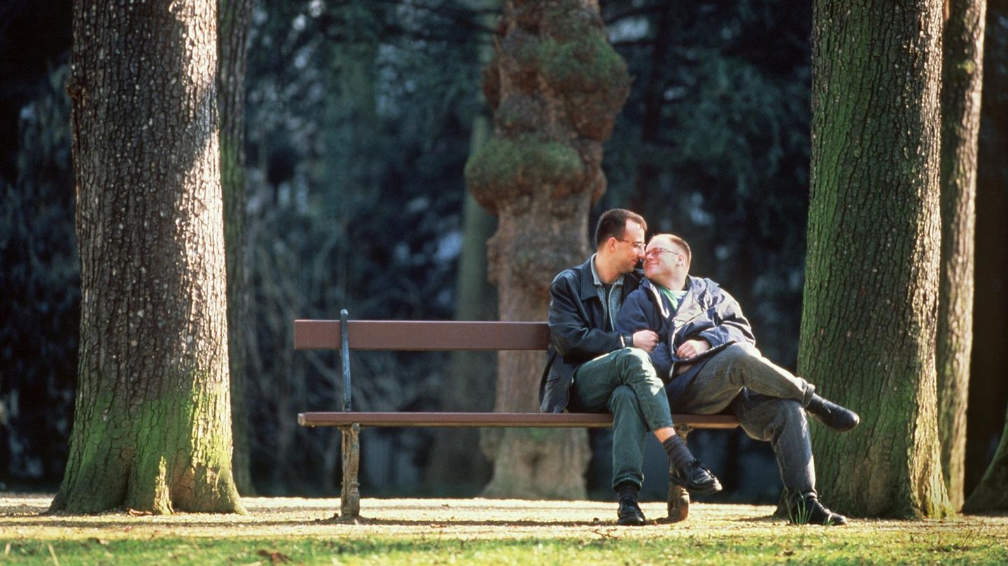 Ein homosexuelles Paar sitzt eng umschlungen auf einer Parkbank.