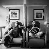 Die Eltern sitzen nebeneinander, währen die Mutter ihre Chemo bekommt