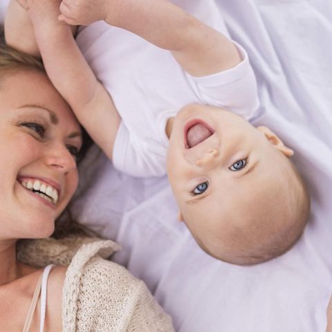 Eine junge Mutter liegt mit einem Baby im Bett (Symbolbild)