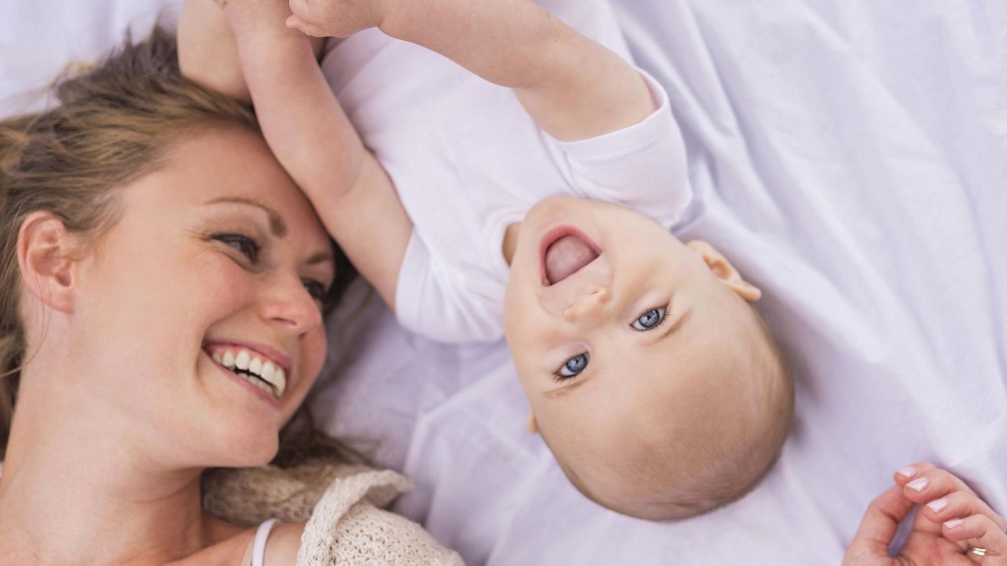 Eine junge Mutter liegt mit einem Baby im Bett (Symbolbild)