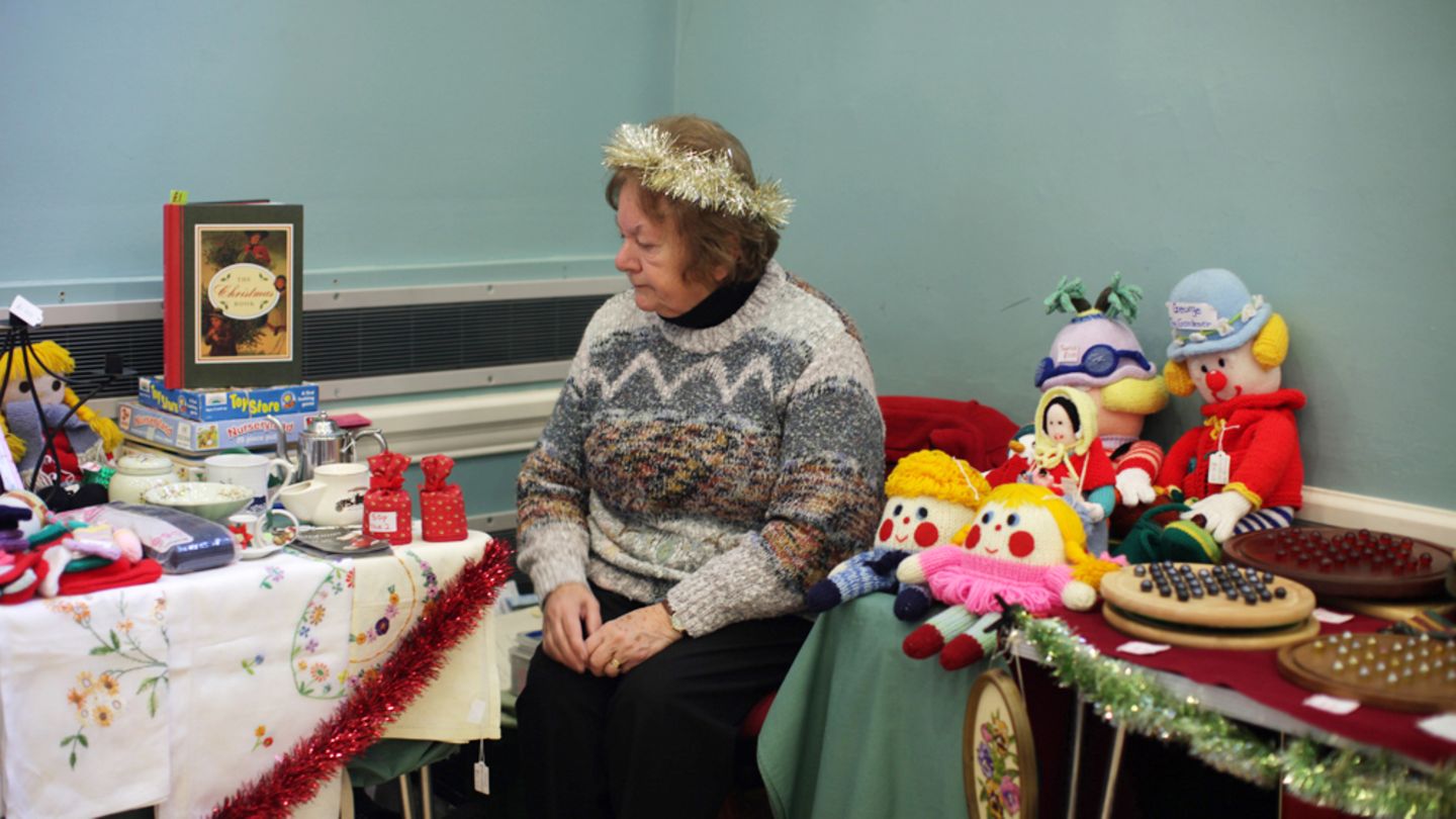 Weihnachtsbazar in Swaffham, Norfolk. Eine Rentnerin bessert sich ihre Pension durch den Verkauf von Nippes auf.