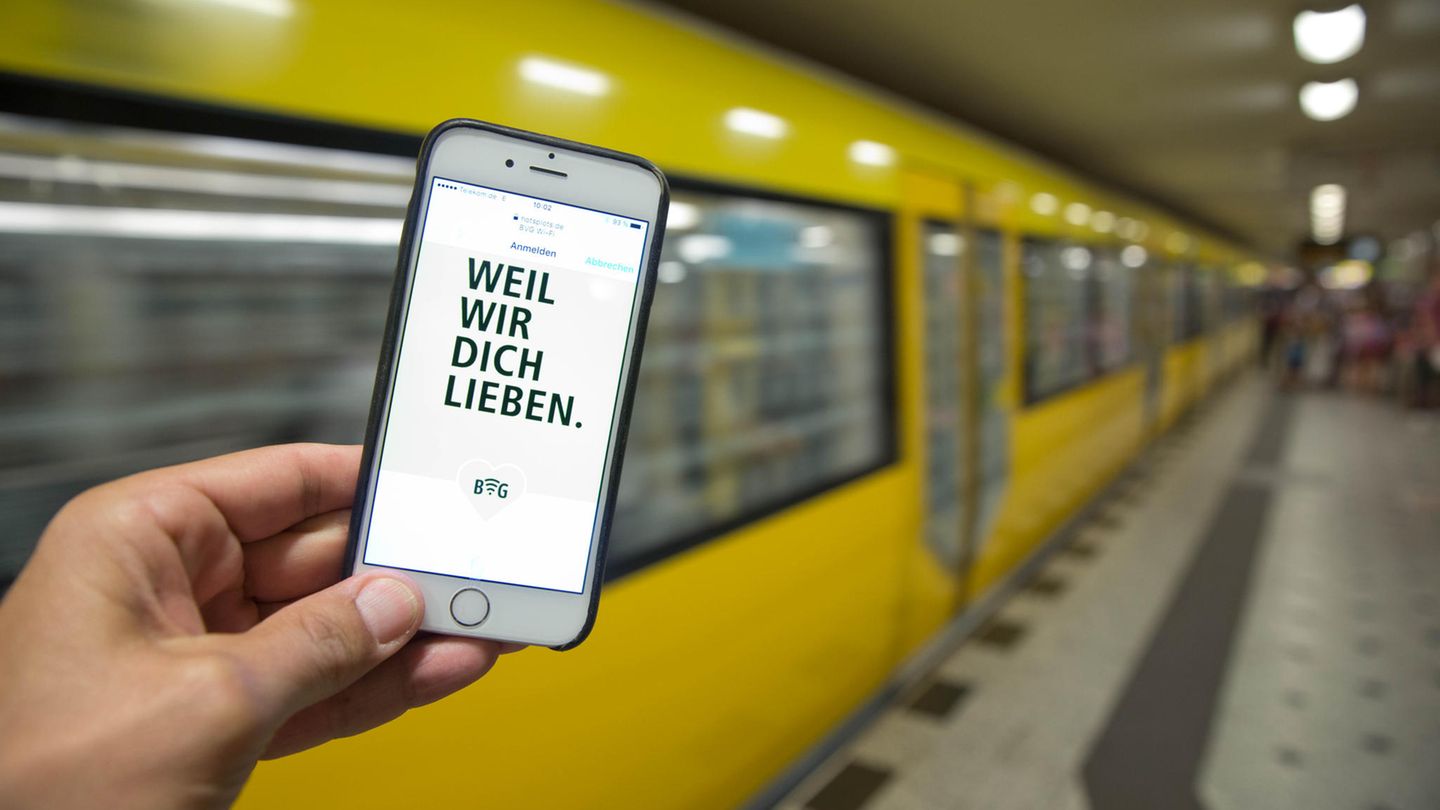 Ein Smartphone mit dem Schriftzug "Weil wir dich lieben" vor einer gelben Berliner U-Bahn