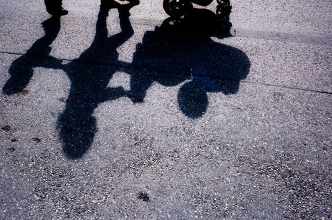 Der Schatten einer Frau, die einen Kinderwagen schiebt und von einem Kleinkind begleitet wird (Symbolbild)