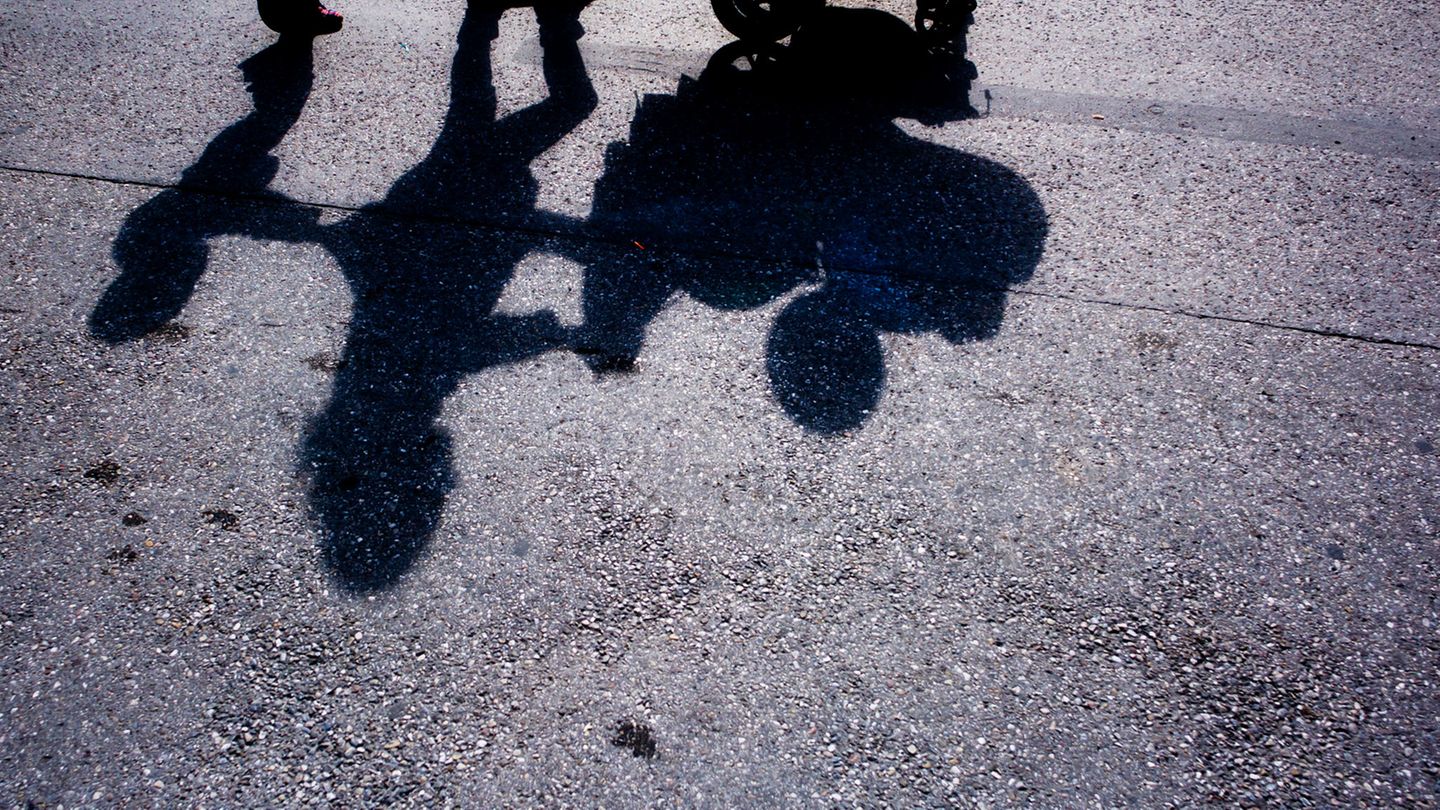 Der Schatten einer Frau, die einen Kinderwagen schiebt und von einem Kleinkind begleitet wird (Symbolbild)