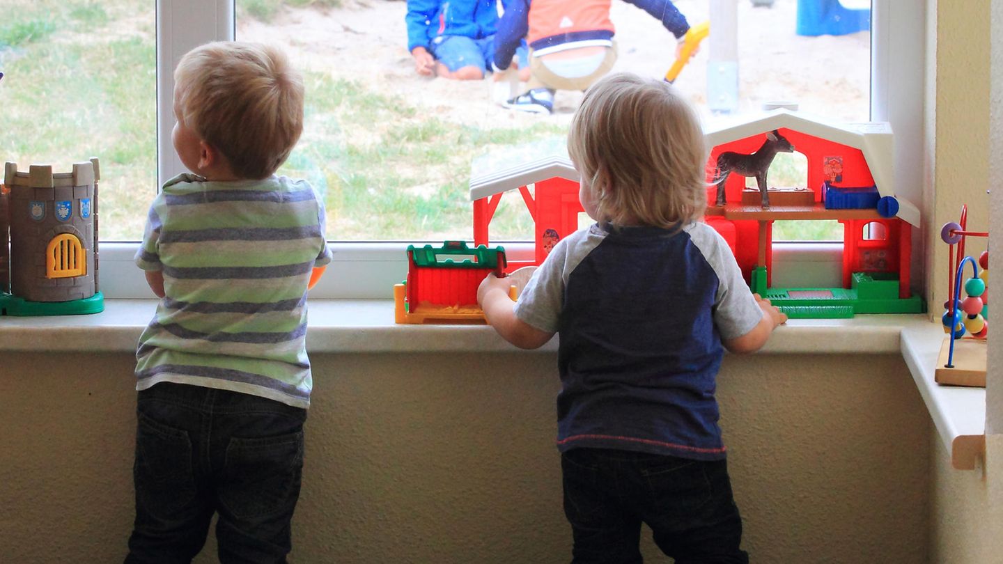 Zwei Kinder schauen aus dem Fenster einer Kita.
