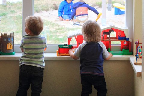 Zwei Kinder schauen aus dem Fenster einer Kita.