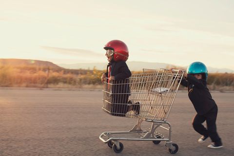 Ein Junge kniet im Einkaufswagen, ein zweiter schiebt, bei tragen einen Motorradhelm