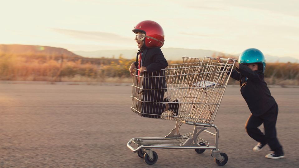 Ein Junge kniet im Einkaufswagen, ein zweiter schiebt, bei tragen einen Motorradhelm