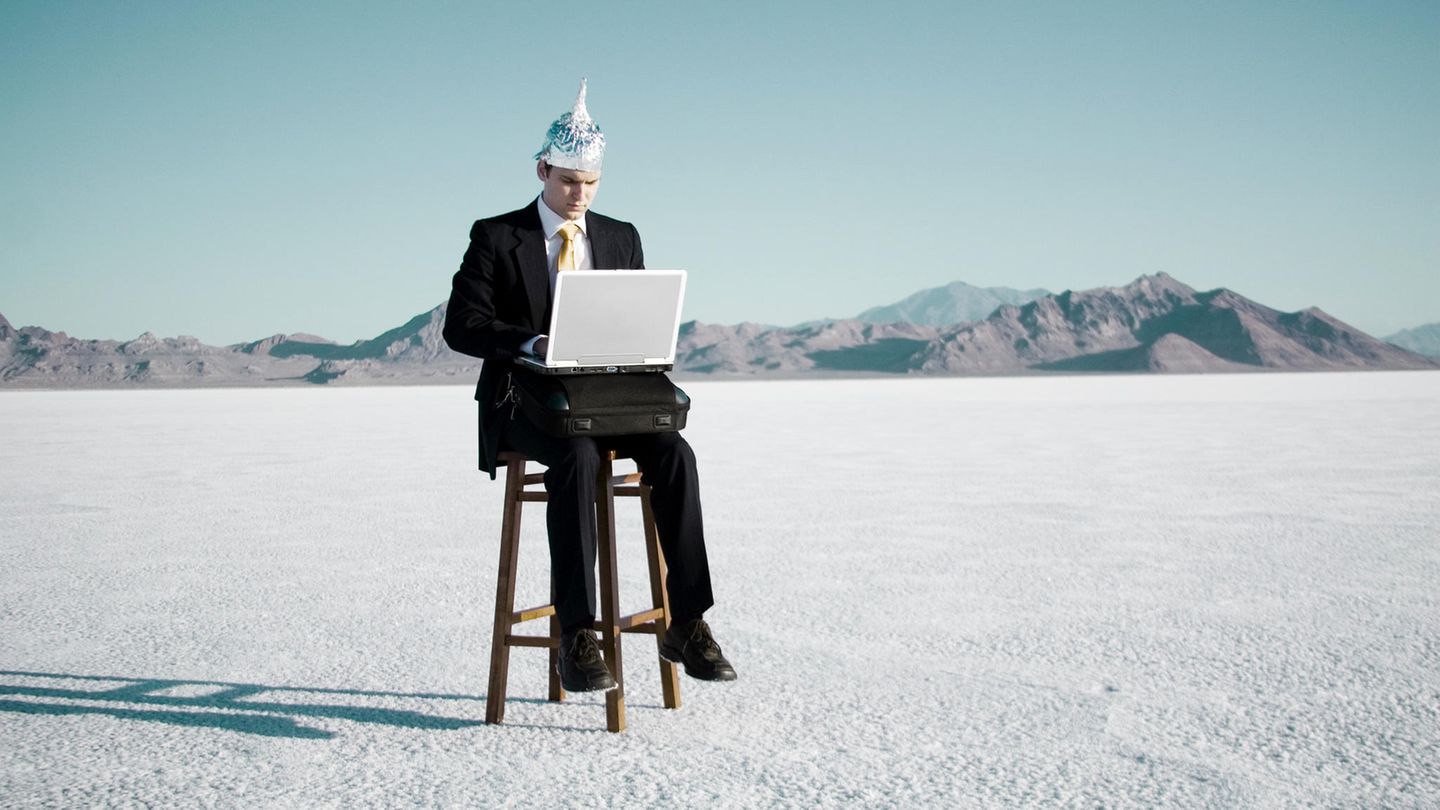 Ein Mann mit Aluhut auf einem Barhocker mit Laptop auf den Knien.