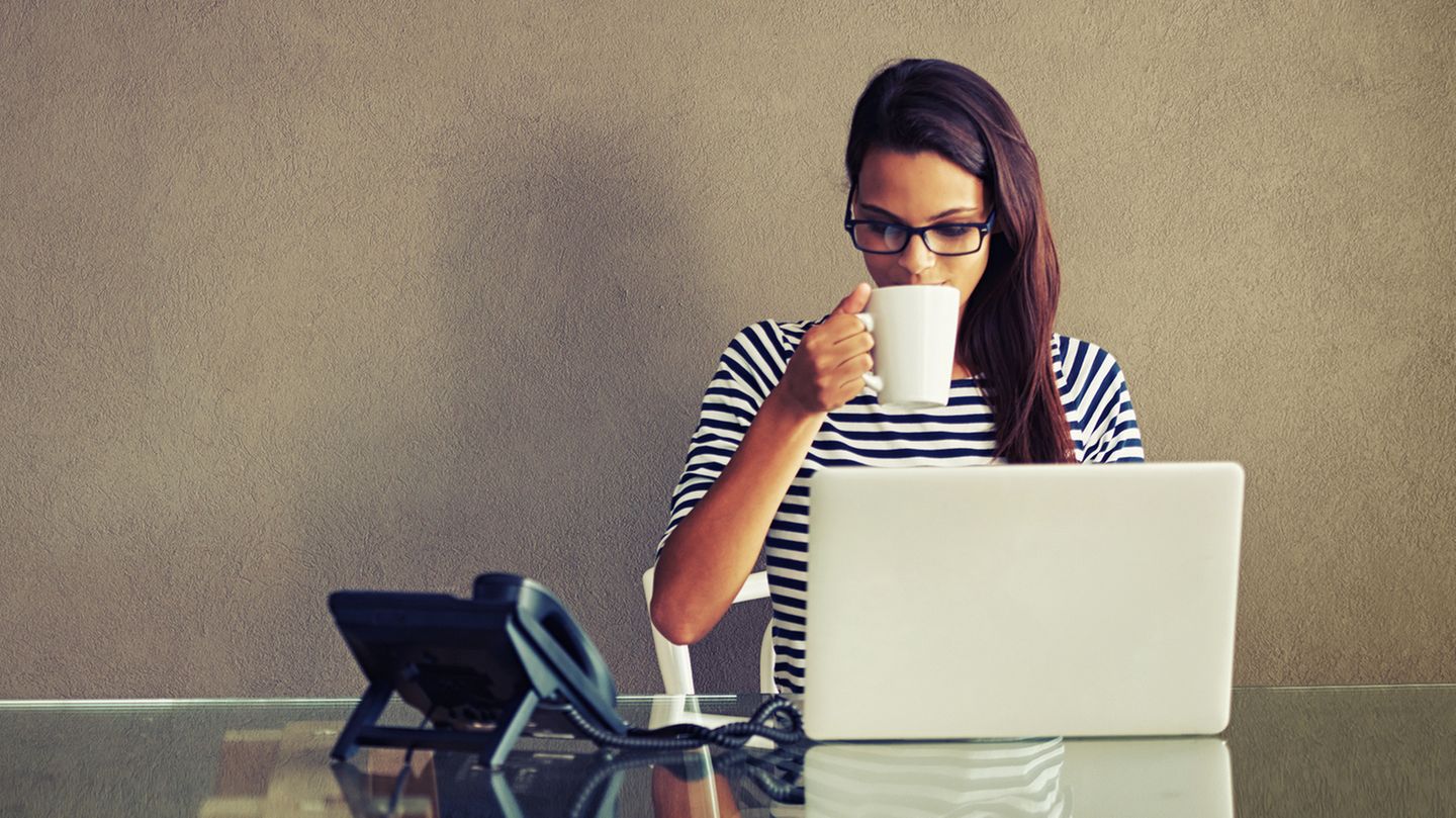 Eine Frau sitzt mit einer Kaffeetasse am Notebook