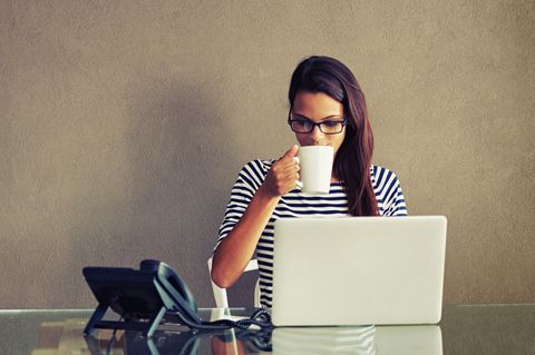 Eine Frau sitzt mit einer Kaffeetasse am Notebook