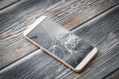 Ein Smartphone liegt mit gerissenem Display auf einem Holzboden
