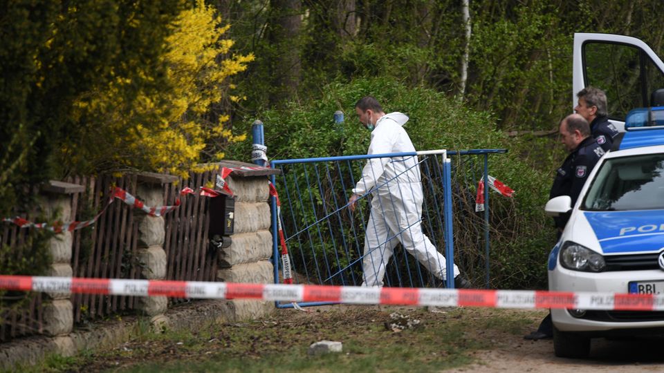Ein Mann im weißen Overall betritt den Tatort in Borkheide - Polizisten warten vor dem Gartentor