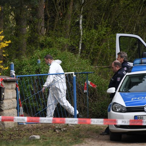 Ein Mann im weißen Overall betritt den Tatort in Borkheide - Polizisten warten vor dem Gartentor