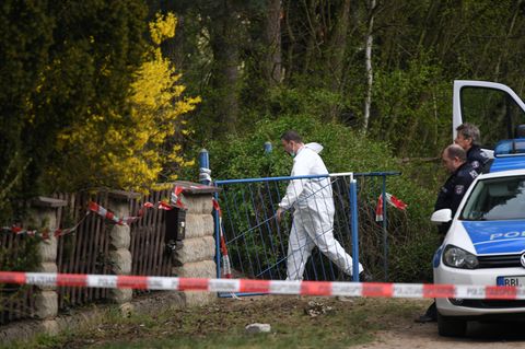 Ein Mann im weißen Overall betritt den Tatort in Borkheide - Polizisten warten vor dem Gartentor