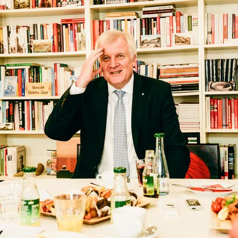 Zu sehen ist Horst Seehofer an einem Tisch mit Getränken und Gebäck. Er fasst sich amüsiert an den Kopf.