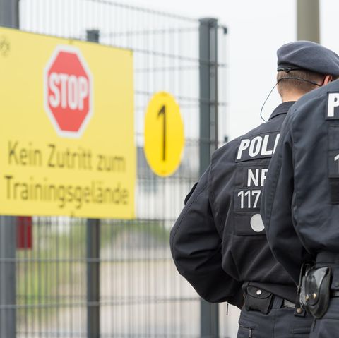 Zwei Polizisten in Kampfmontur gehen bei Borussia Dortmund am Schild vorbei, das das Betreten des Trainingsgeländes verbietet