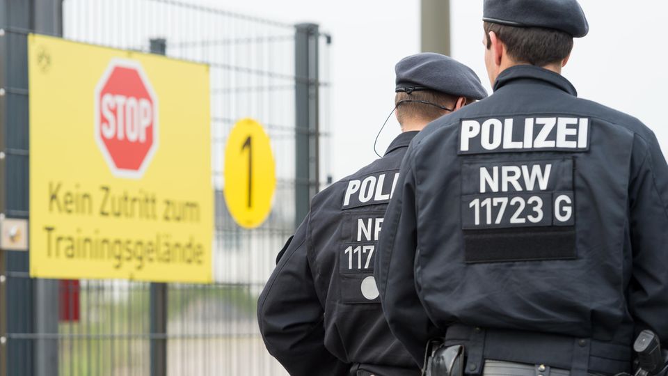 Zwei Polizisten in Kampfmontur gehen bei Borussia Dortmund am Schild vorbei, das das Betreten des Trainingsgeländes verbietet