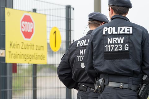Zwei Polizisten in Kampfmontur gehen bei Borussia Dortmund am Schild vorbei, das das Betreten des Trainingsgeländes verbietet