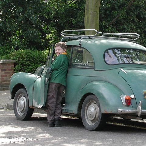 Junge steht neben einen Auto und lacht