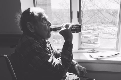 Ein alter Mann sitzt am Fenster und trinkt ein Bier aus der Flasche