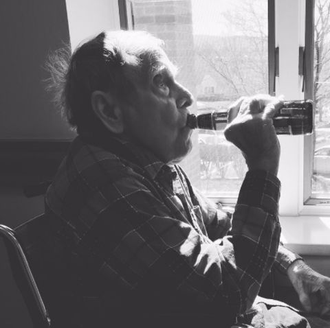 Ein alter Mann sitzt am Fenster und trinkt ein Bier aus der Flasche