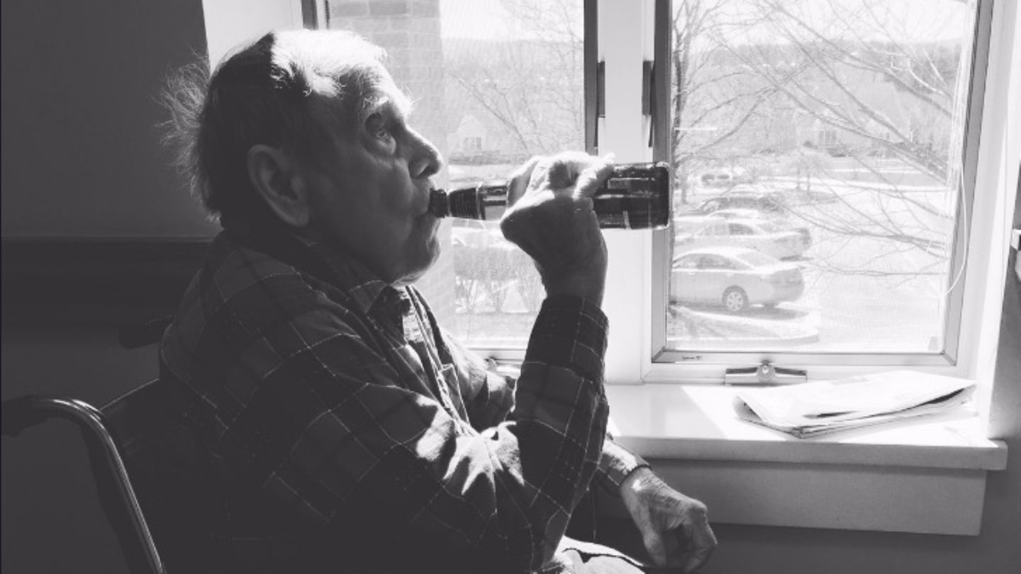 Ein alter Mann sitzt am Fenster und trinkt ein Bier aus der Flasche
