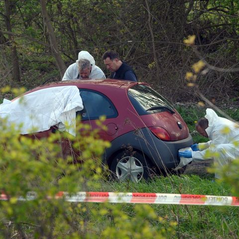 Männer in weißen Overalls untersuchen einen roten Ford Ka - Weißes Tuch deckt den Vorderbereich ab