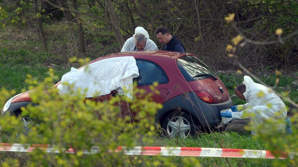 Männer in weißen Overalls untersuchen einen roten Ford Ka - Weißes Tuch deckt den Vorderbereich ab