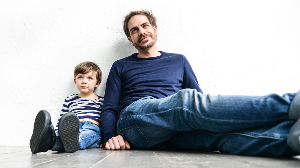 Vater und Sohn Vater und Sohn sitzen auf dem Boden, an eine Wand angelehnt