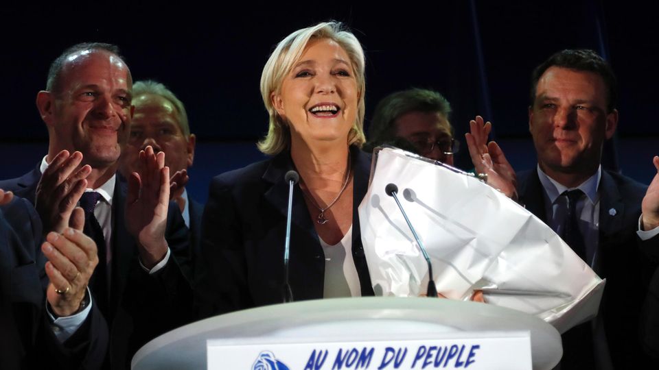 Marine Le Pen steht bei der Präsidentschaftswahl mit einem Strauß Blumen im Arm lächelnd hinter einem Rednerpult