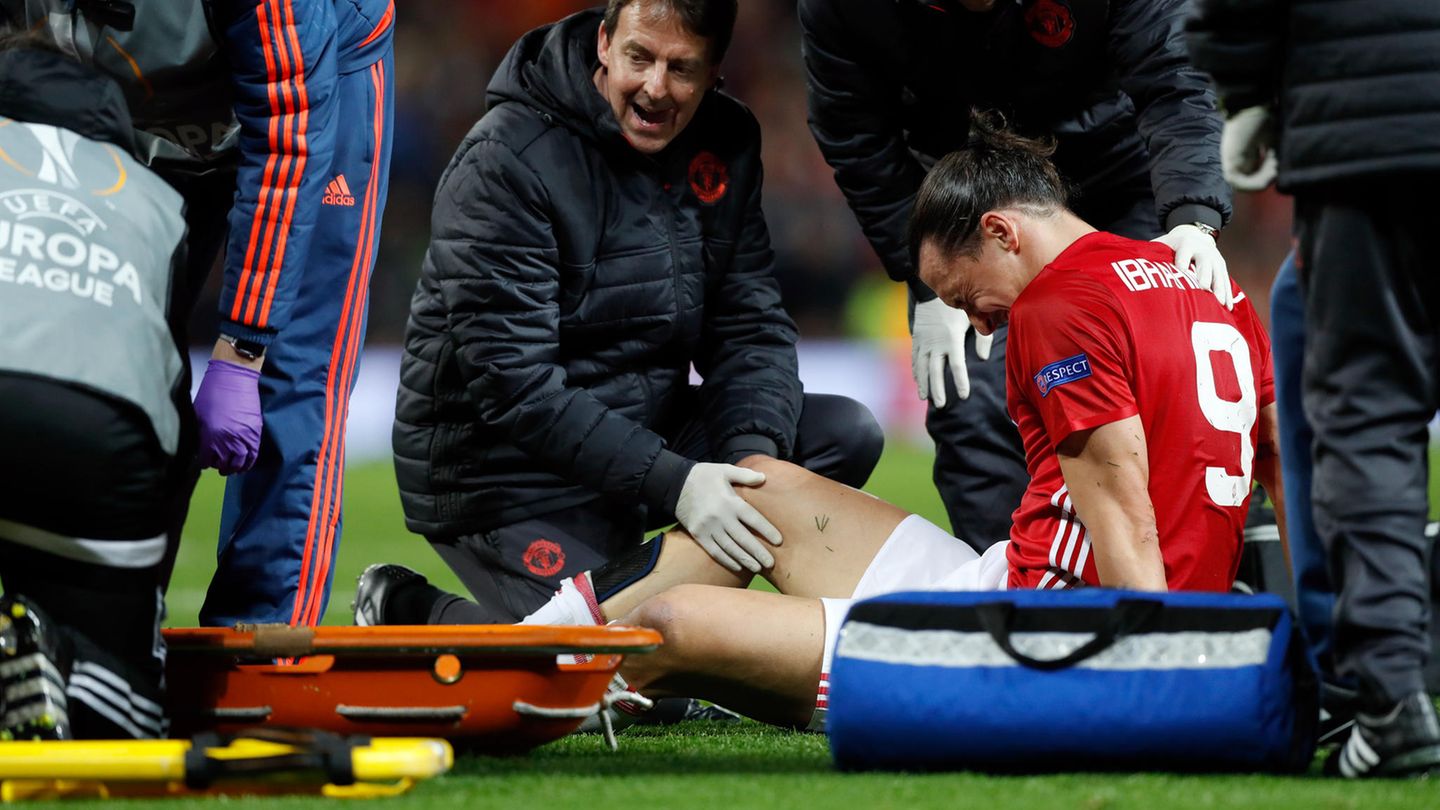 Zlatan Ibrahimovic sitzt mit schmerzverzerrtem Gesicht auf dem Rasen, während ein Betreuer sein rechtes Knie untersucht.