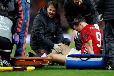 Zlatan Ibrahimovic sitzt mit schmerzverzerrtem Gesicht auf dem Rasen, während ein Betreuer sein rechtes Knie untersucht.