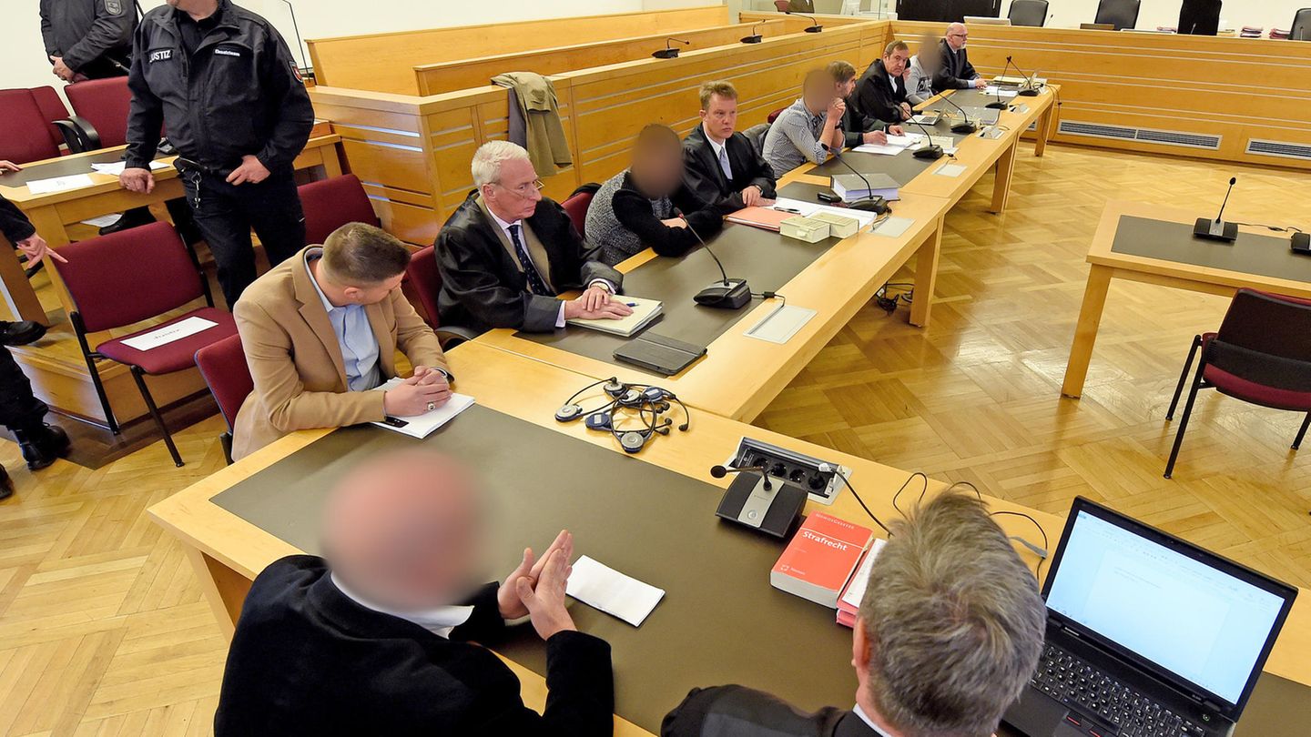 Die Angeklagten mit ihren Verteidigern beim Prozessauftakt in Hannover. Polizisten sichern den Gerichtssaal und das Gebäude.