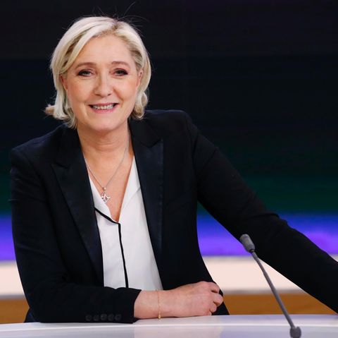 Marine Le Pen sitzt in einem Fernsehstudio vor einer blauschwarzen Wand und lächel