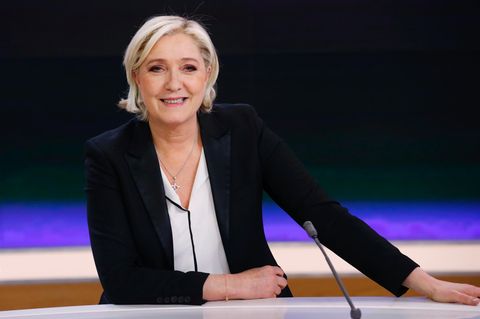 Marine Le Pen sitzt in einem Fernsehstudio vor einer blauschwarzen Wand und lächel