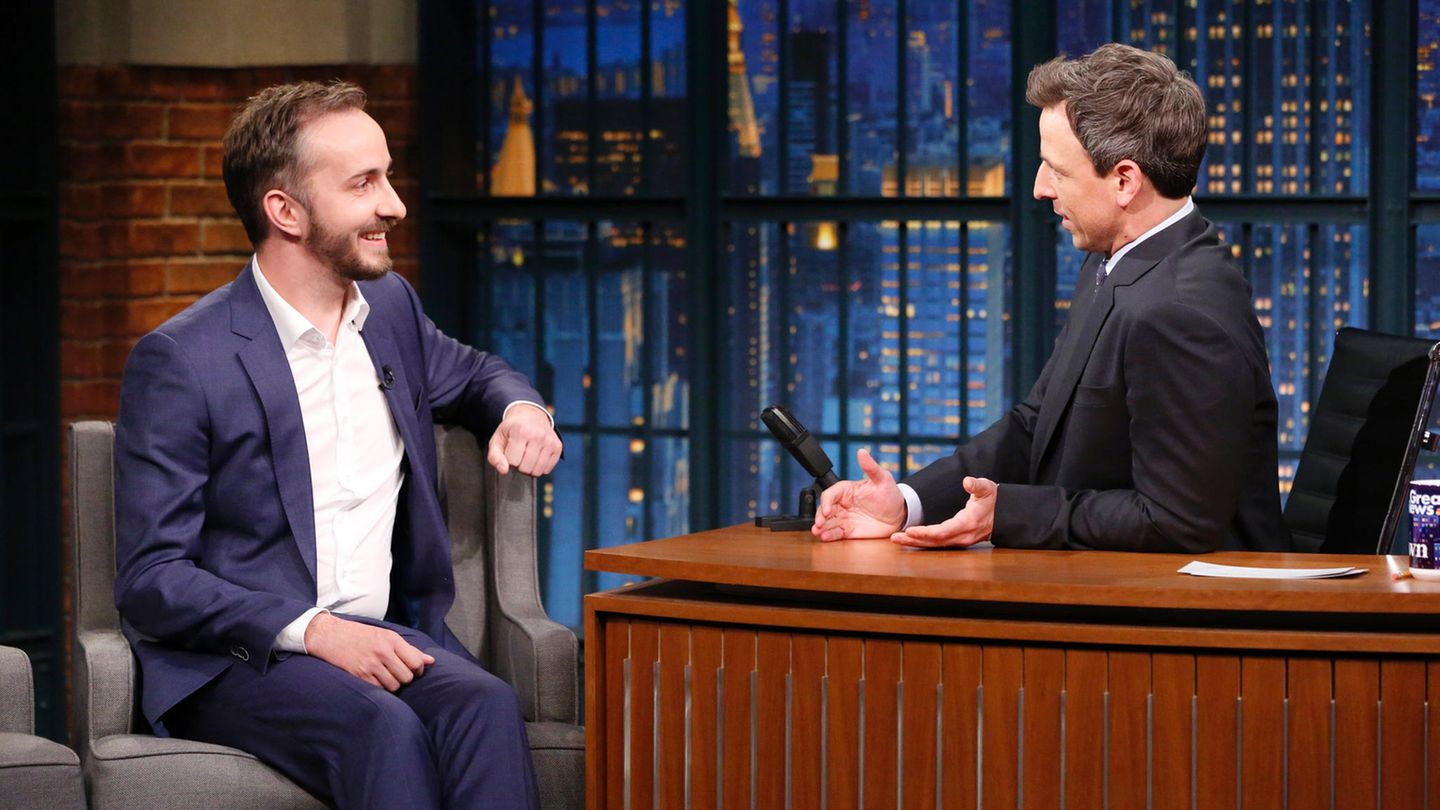 Jan Böhmermann sitzt links auf einem Sessel, während Moderator Seth Meyers hinter seinem hölzernen Schreibtisch sitzt