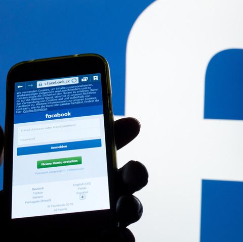 Ein Smartphone Display mit der Login-Seite von Facebook leuchtet vor einer Wand mit einem großen Facebook-Logo