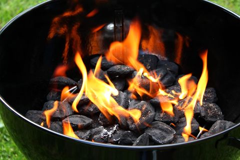 Flammen schlagen zwischen der Holzkohle in einem Kugelgrill