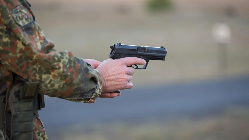 Ein Bundeswehrsoldat in Tarnfleck-Uniform hält mit beiden Händen eine Pistole