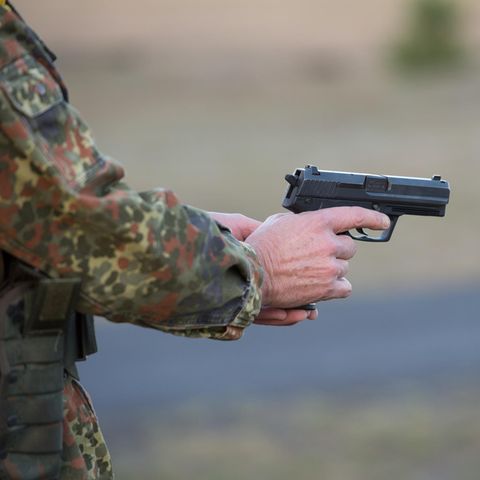 Ein Bundeswehrsoldat in Tarnfleck-Uniform hält mit beiden Händen eine Pistole