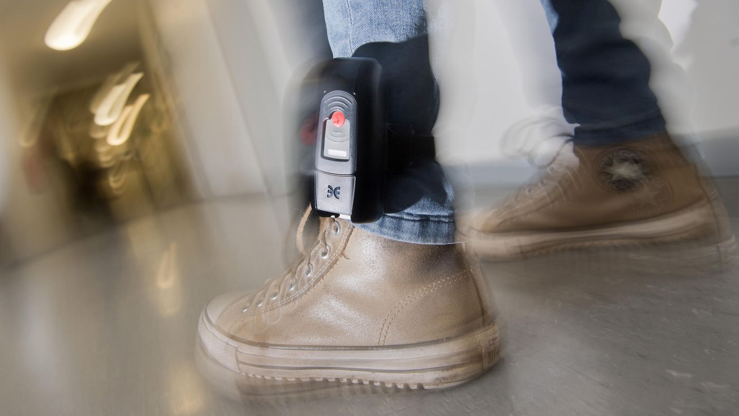 Am linken Bein eines Mannes ist über einer Jeans eine elektronische Fußfessel zu sehen
