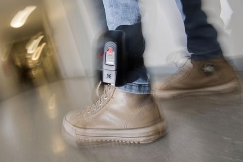 Am linken Bein eines Mannes ist über einer Jeans eine elektronische Fußfessel zu sehen