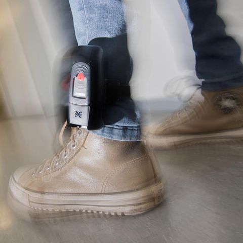Am linken Bein eines Mannes ist über einer Jeans eine elektronische Fußfessel zu sehen