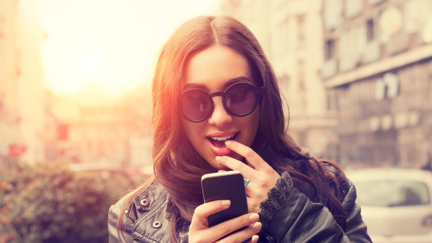 Eine junge Frau betrachtet aufgeregt ihr Smartphone