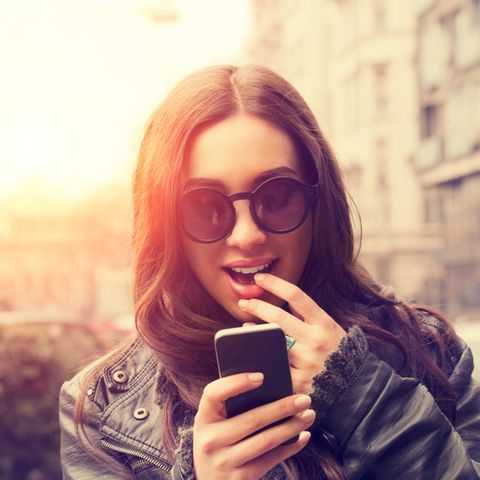 Eine junge Frau betrachtet aufgeregt ihr Smartphone