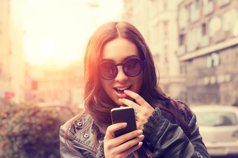 Eine junge Frau betrachtet aufgeregt ihr Smartphone