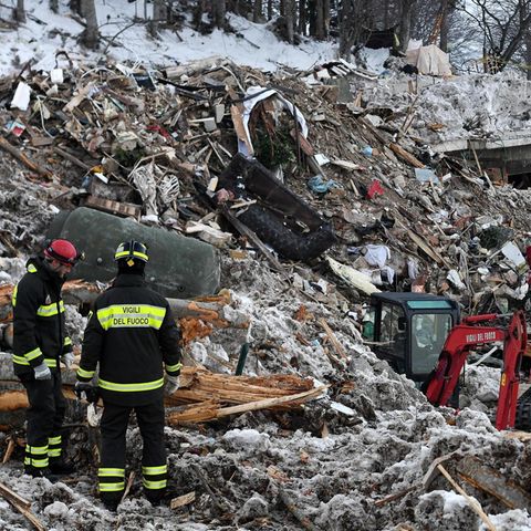 Zwei Feuerwehrmänner und ein Bagger stehen auf den Trümmern des von einer Lawine verschütteten Hotels Rigopiano in den Abruzzen