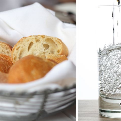 Ein Brotkorb und ein Glas Wasser stehen auf einem Tisch.